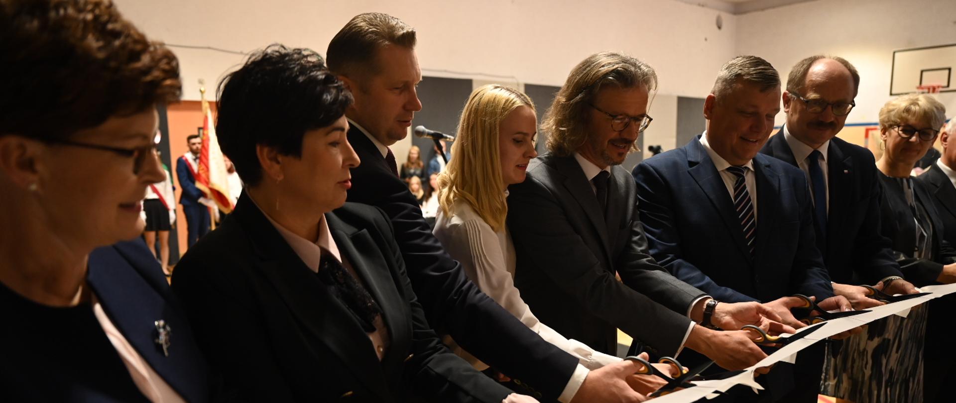 Kilka osób stoi przy wstędze, przecinają ją nożyczkami.