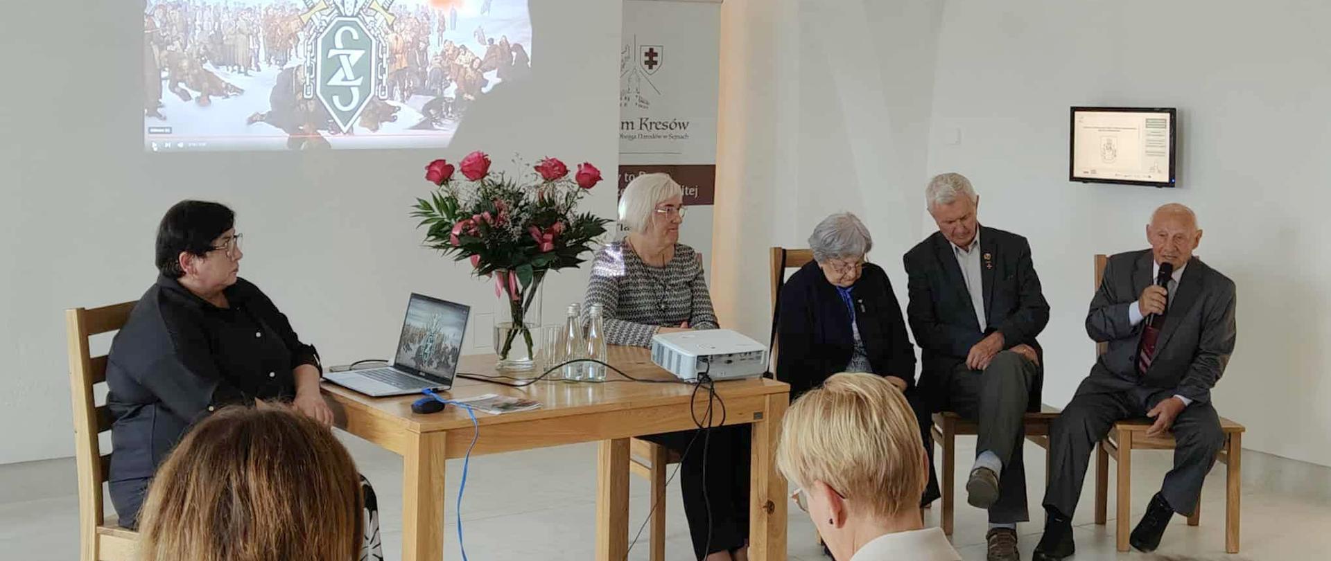 Grupa starszych osób siedzących na krzesłach przed widownią