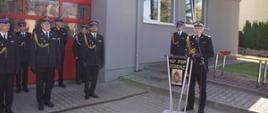 Na zdjęciu widać przemawiającego zastępce Komendanta Głównego PSP - nadbrygadiera Krzysztofa Hejduka, na tle przedniej części Jednostki Ratowniczo-Gaśniczej w Zgierzu.