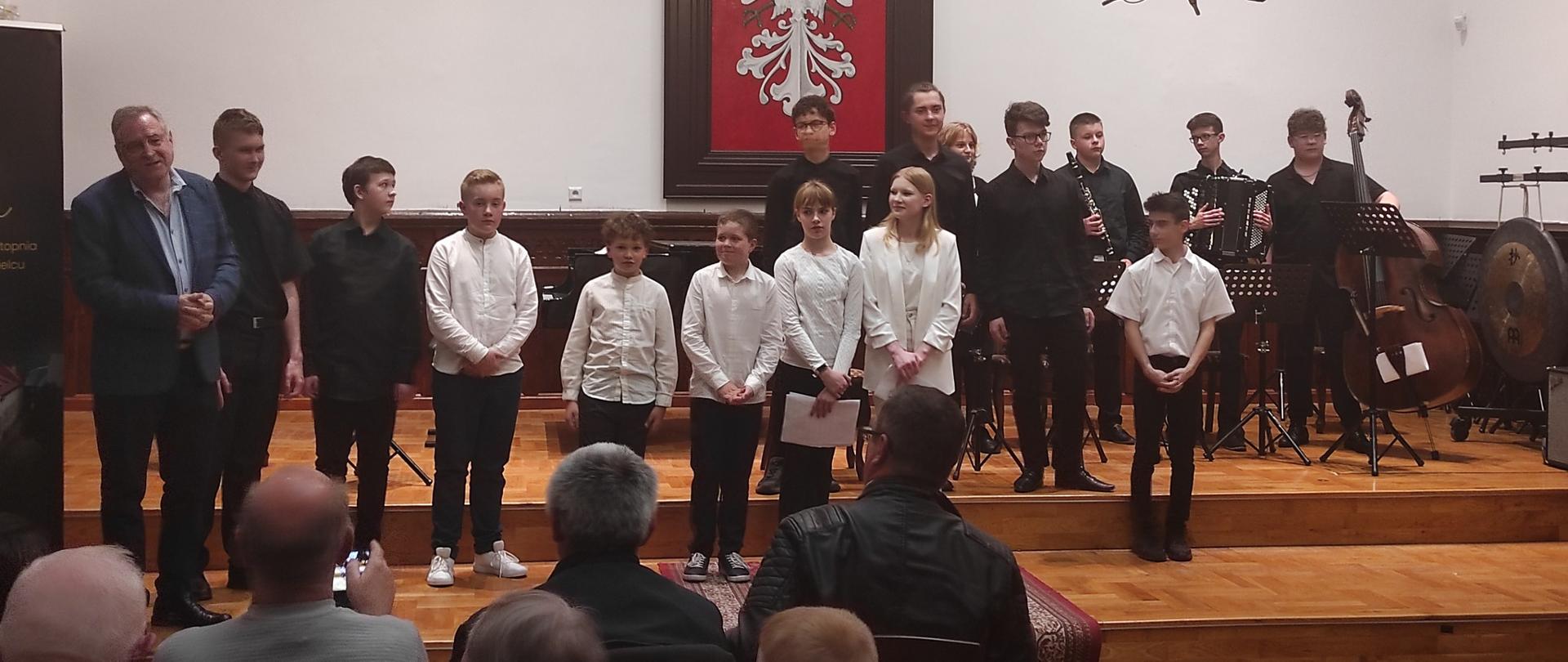 uczniowie klasy akordeonu wraz ze swoim nauczycielem zgromadzeni na scenie w Sali Królewskiej PSM Mielec podczas swojego koncertu klasowego 