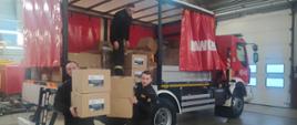 Zdjęcie przedstawia trzech strażaków zdejmujących pudła z samochodu kwatermistrzowskiego 