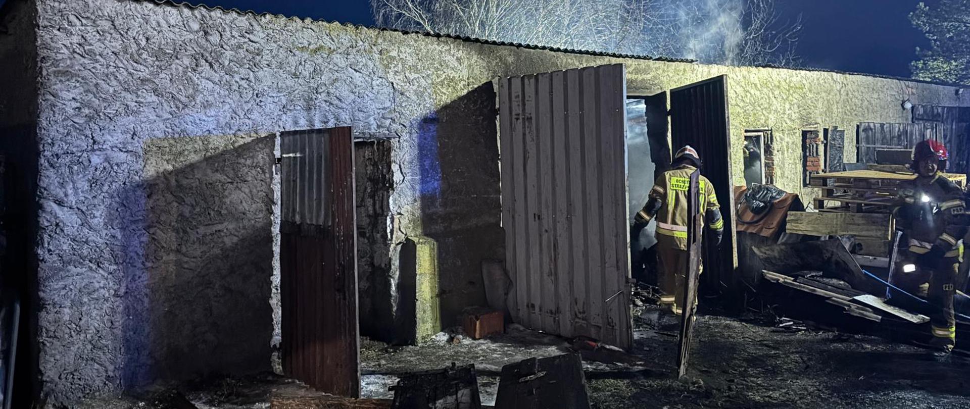 Na zdjęciu widać strażaków w trakcie działań gaśniczych, budynku gospodarczego. 