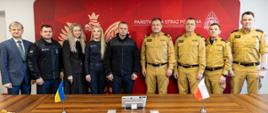 Spotkanie ze strażakami z Obwodu Iwanofrankiwskiego, których w sali sztabowej Komendy Wojewódzkiej Państwowej Straży Pożarnej w Opolu przywitał Opolski Komendant Wojewódzki PSP nadbryg. Paweł Kielar, Zastępca Opolskiego Komendanta Wojewódzkiego PSP st. bryg. Arkadiusz Kuśmierski, Zastępca Opolskiego Komendanta Wojewódzkiego PSP st. bryg. Piotr Dudek oraz Zastępca Komendanta Miejskiego PSP w Opolu mł. bryg. Piotr Bibułowicz. W tle strażaków czerwony banner Państwowej Straży Pożarnej z białym herbem Polski. Wspólne zdjęcie grupowe uczestników spotkania.
