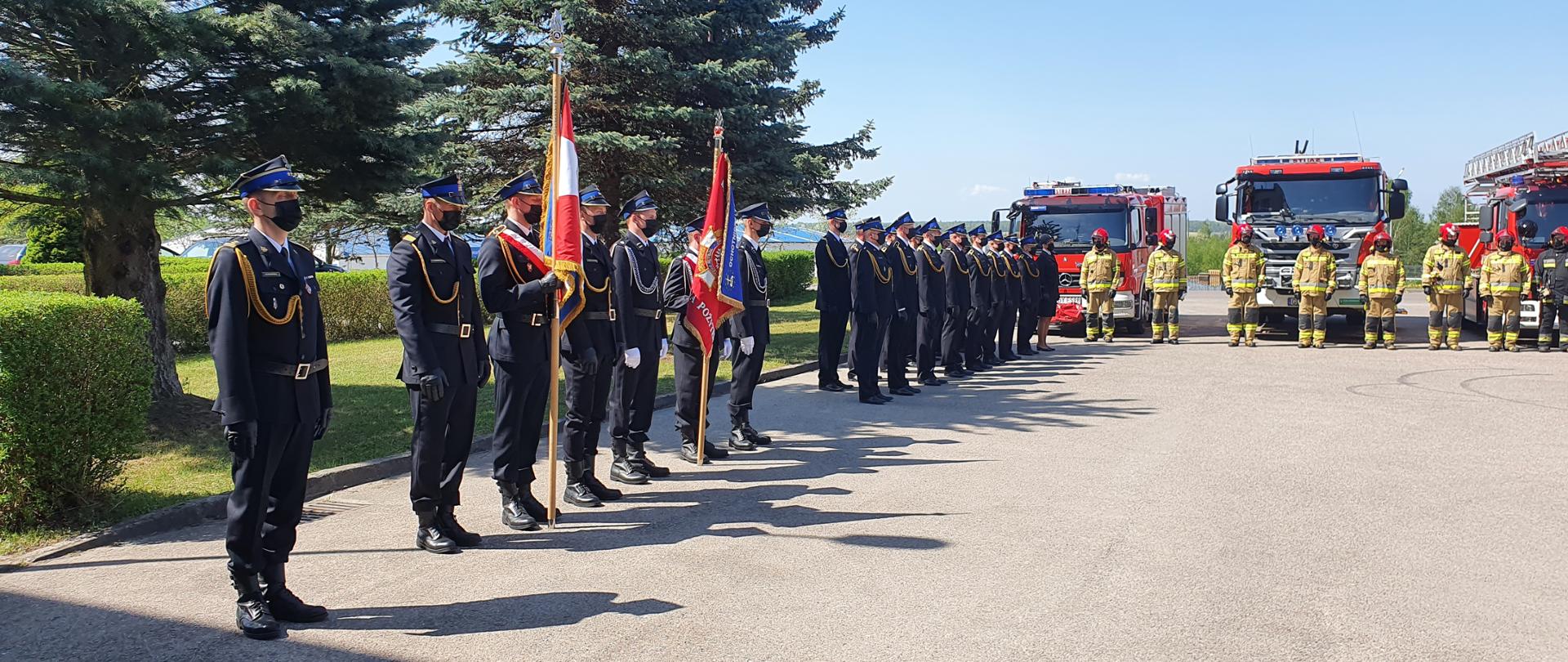 Na zdjęciu znajdują się 2 poczty sztandarowe, pododdział umundurowanych funkcjonariuszy Komendy Powiatowej PSP w Bytowie stojących w dwuszeregu. Za pododdziałem ustawiony jest samochód ratowniczo-gaśniczy JRG Nr 1 w Bytowie. 