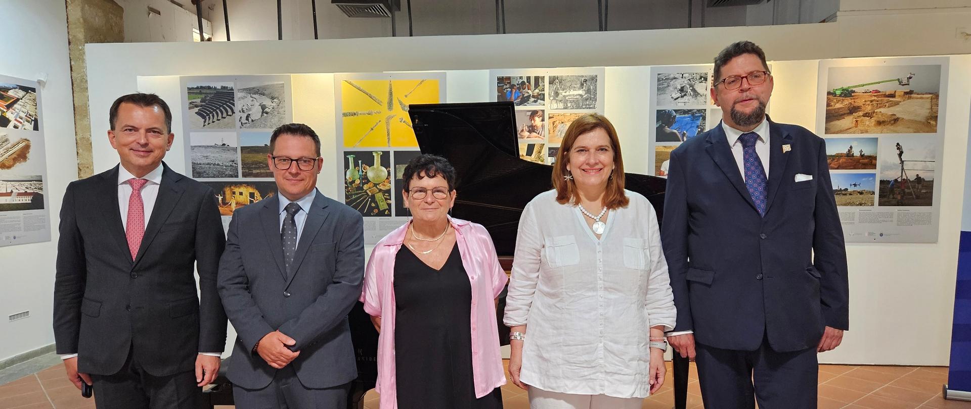 W sali stoi w rzędzie pięć osób, dwóch mężczyzn w garniturach, dwie kobiety i wiceminister Szeptycki, za nimi czarny fortepian.