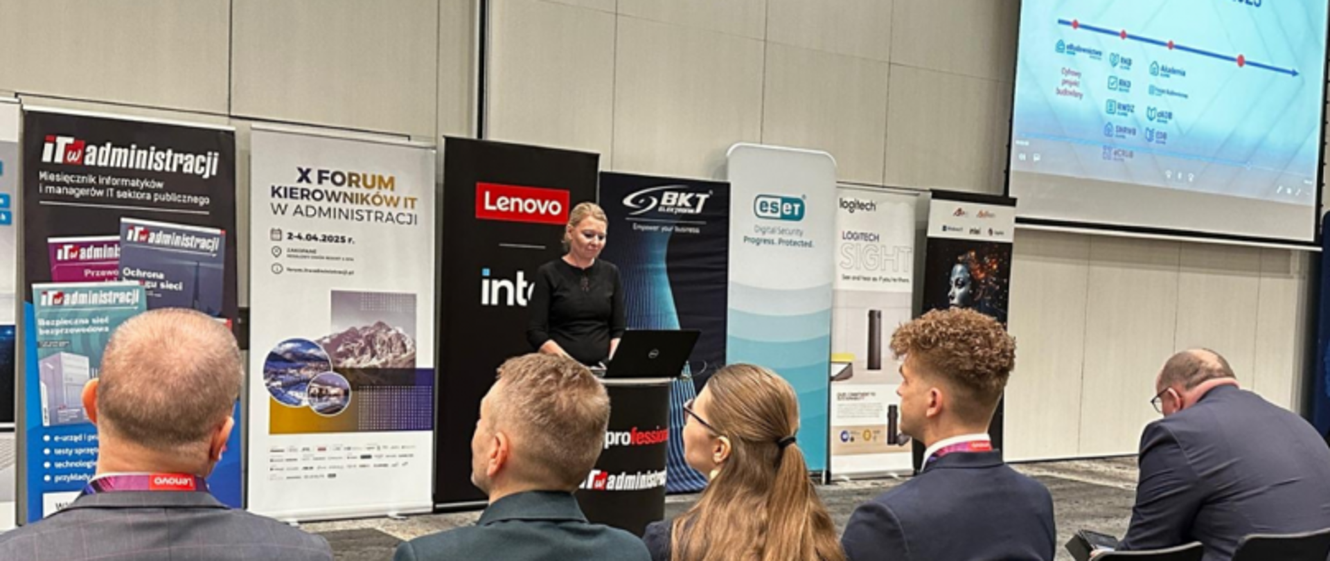 Dorota Cabańska z Głównego Inspektoratu Nadzoru Budowlanego (GINB) wygłasza prezentację na X Forum Kierowników IT w Administracji; na sali siedzi kilku uczestników, w tle widoczne są banery sponsorów i ekran z prezentacją.