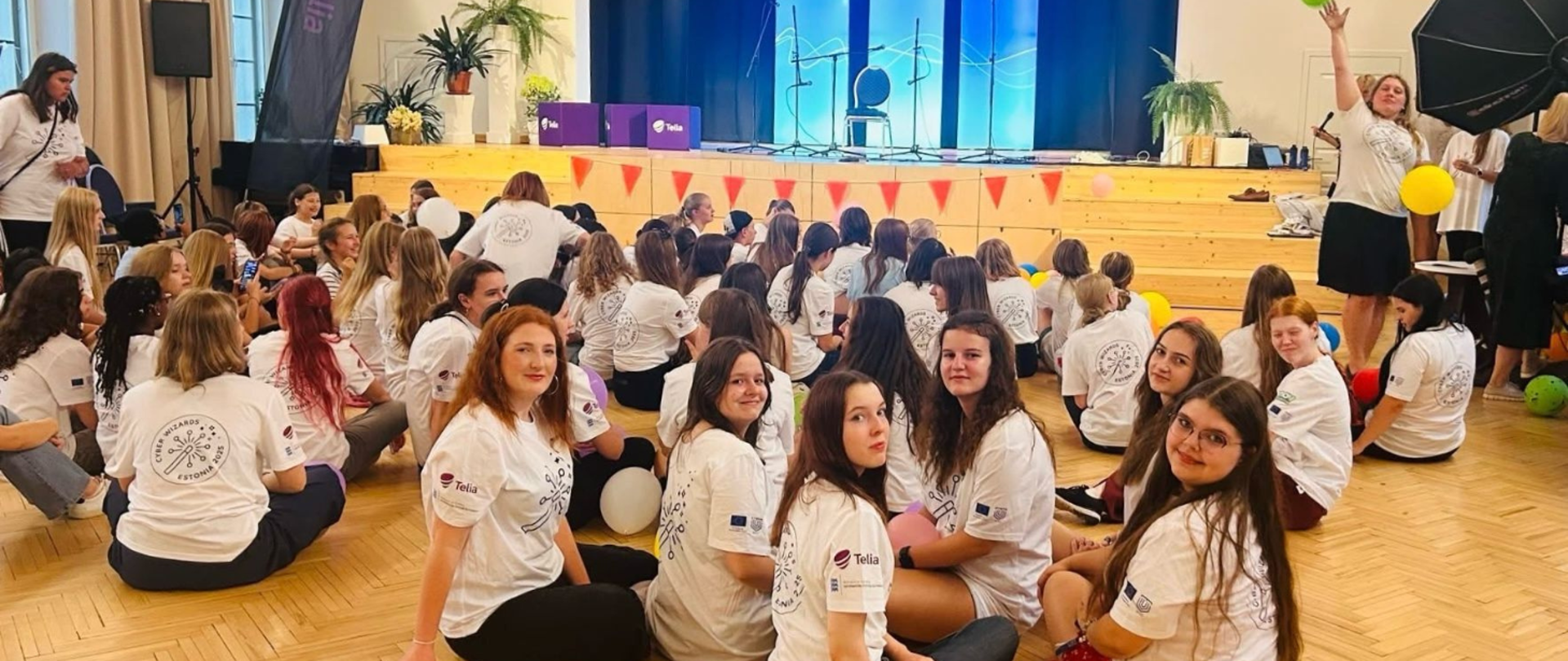 Grupa dziewcząt siedzi na podłodze dużej sali