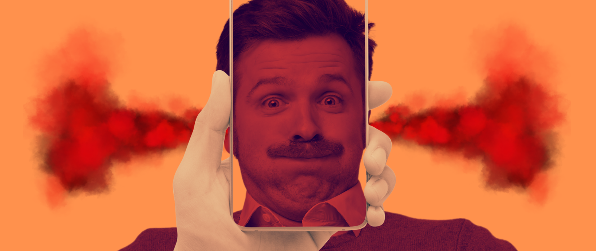 Mężczyzna z poczerwieniałą twarzą zatrzymuje powietrze w ustach i wytrzeszcza oczy. Z uszu wylatuje mu dym. Jego twarz widziana przez ekran trzymanego w dłoni smartfona.