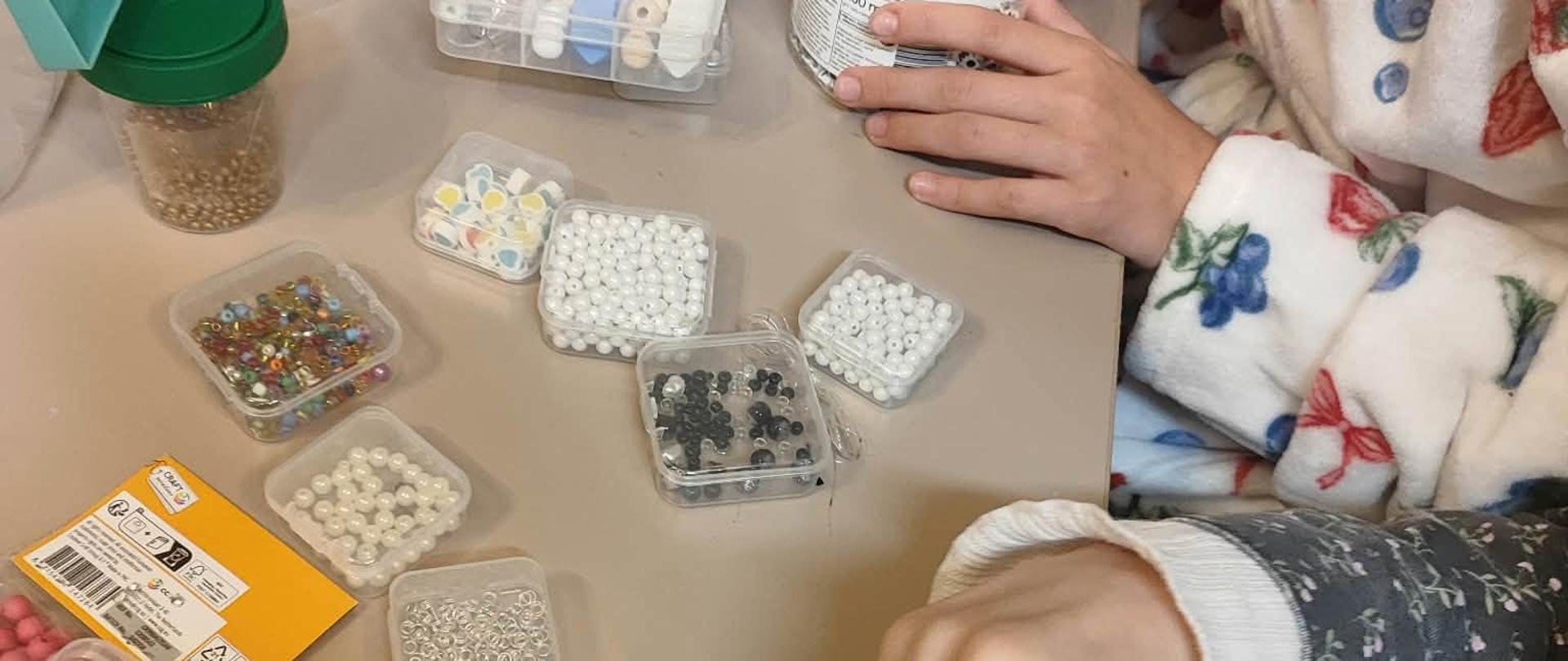 Zdjęcie stołu przy którym siedzą dziewczynki i wykonują ręcznie ozdoby z kolorowych koralików