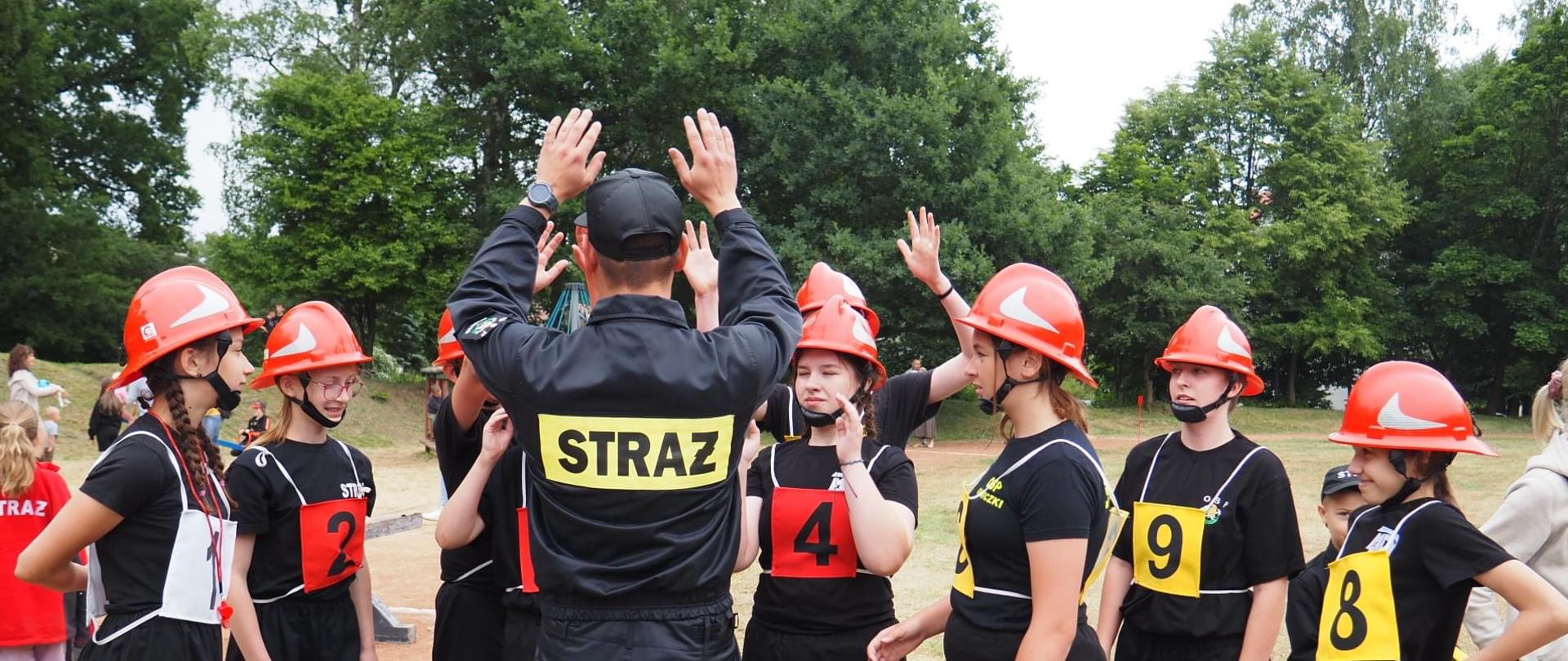Członkowie Młodzieżowej Drużyny Pożarniczej przybijają piątki ze strażakiem OSP.