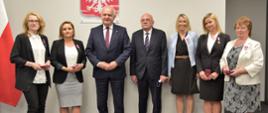Do wspólnego zdjęcia pozuje 5 odznaczonych pań z medalami przypiętymi do klap marynarek. Wraz z nimi stoi wojewoda i dyrektor inspekcji handlowej. 