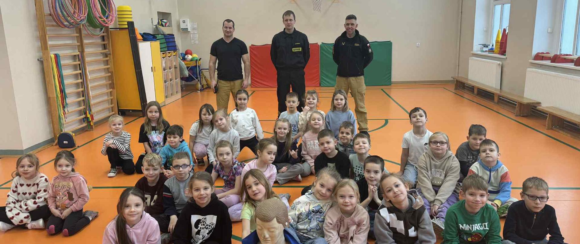 Aktywni Błękitni 1 - zdjęcie przedstawia dzieci na sali za nimi stoją strażacy