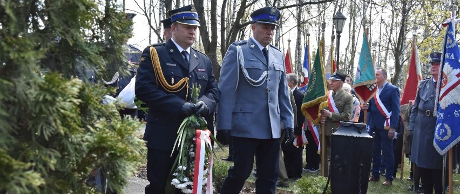 Na zdjęciu zastępca komendanta KP PSP Śrem wraz z funkcjonariuszem policji podczas składania wiązanki kwiatów pod pomnikiem z boku stoją poczty sztandarowe