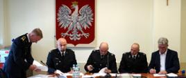 Zdjęcie przedstawia przedstawicieli straży państwowej i osp oraz władze miasta podpisujących dokumenty w biurze. 