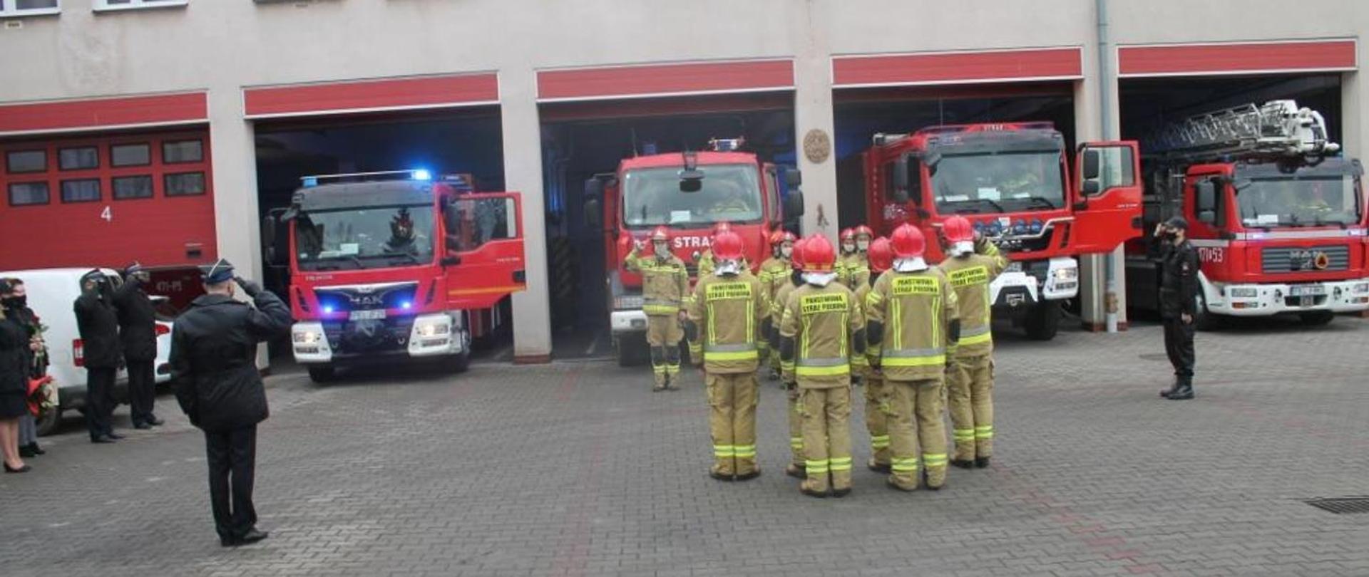 Uroczysta zbiórka strażaków na placu przed strażnicą. Strażacy w maseczkach.