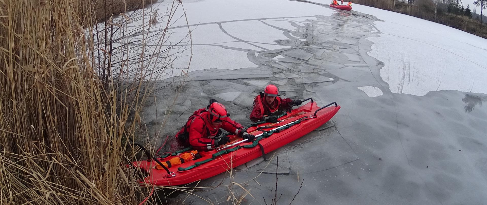 Zdjęcie przedstawia ćwiczenia doskonalenia zawodowego na zbiorniku wodnym. Na zdjęciu widać ratowników przygotowujących się do ćwiczeń z zakresu wodno- lodowych. Zdjęcie wykonane w porze dziennej na zbiorniku wodnym.