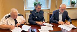 Zdjęcie przedstawia trzech mężczyzn podpisujących dokumenty. Na zdjęciu znajduje się Komendant Powiatowy PSP w Brzegu, Burmistrz Grodkowa i Prezes OSP Wierzbnik.