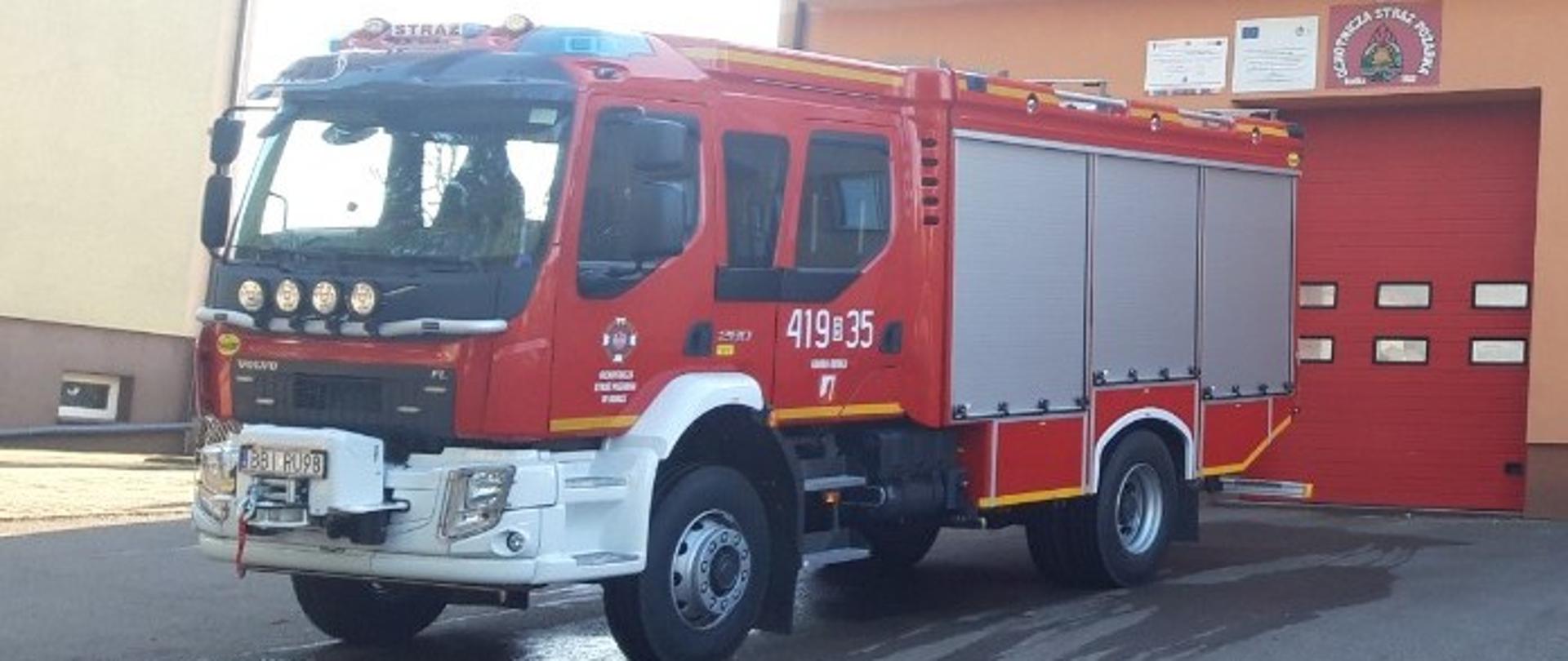 Widok na nowy samochód ratowniczo-gaśniczy dla Ochotniczej Straży Pożarnej w Rudce na tle strażnicy.