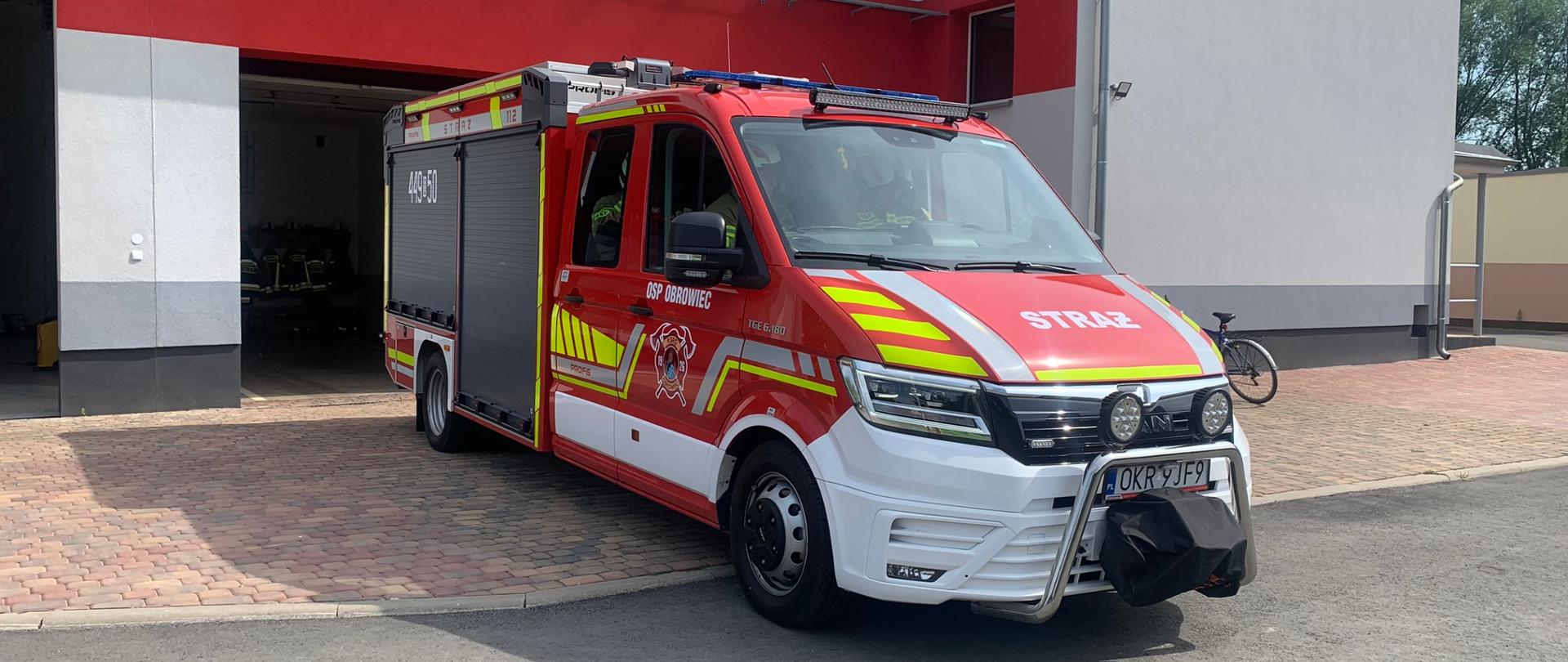 Na tle remizy OSP ustawiony przed garażem samochód pożarniczy. 