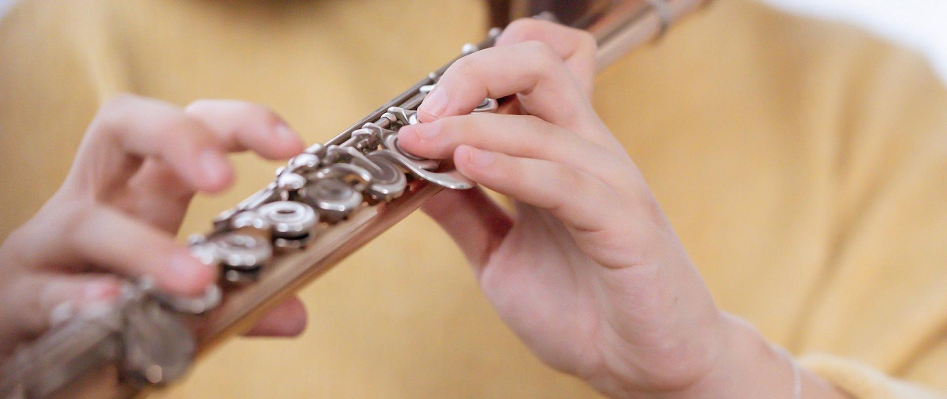 Zdjęcie przedstawiające zbliżenie na dłonie grającej flecistki ubranej na żółto