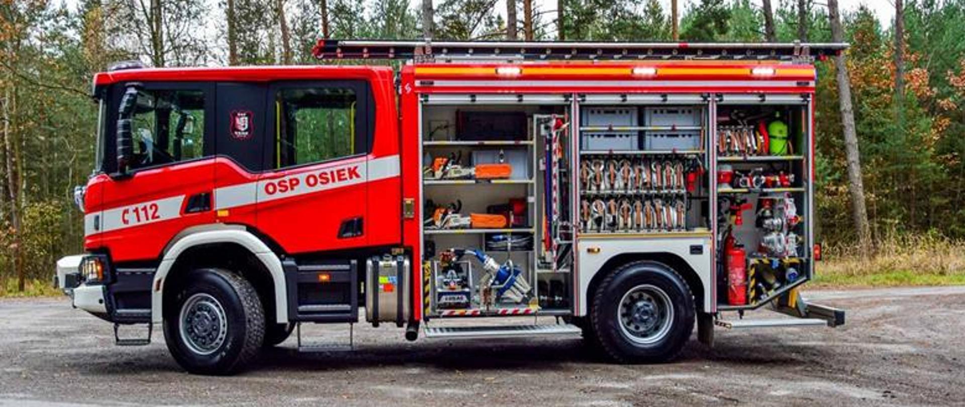 Zdjęcie przedstawia ciężki samochód ratowniczo-gaśniczy zna podwoziu Man. Pojazd prezentuje zamontowane wyposażenie w skrytkach.