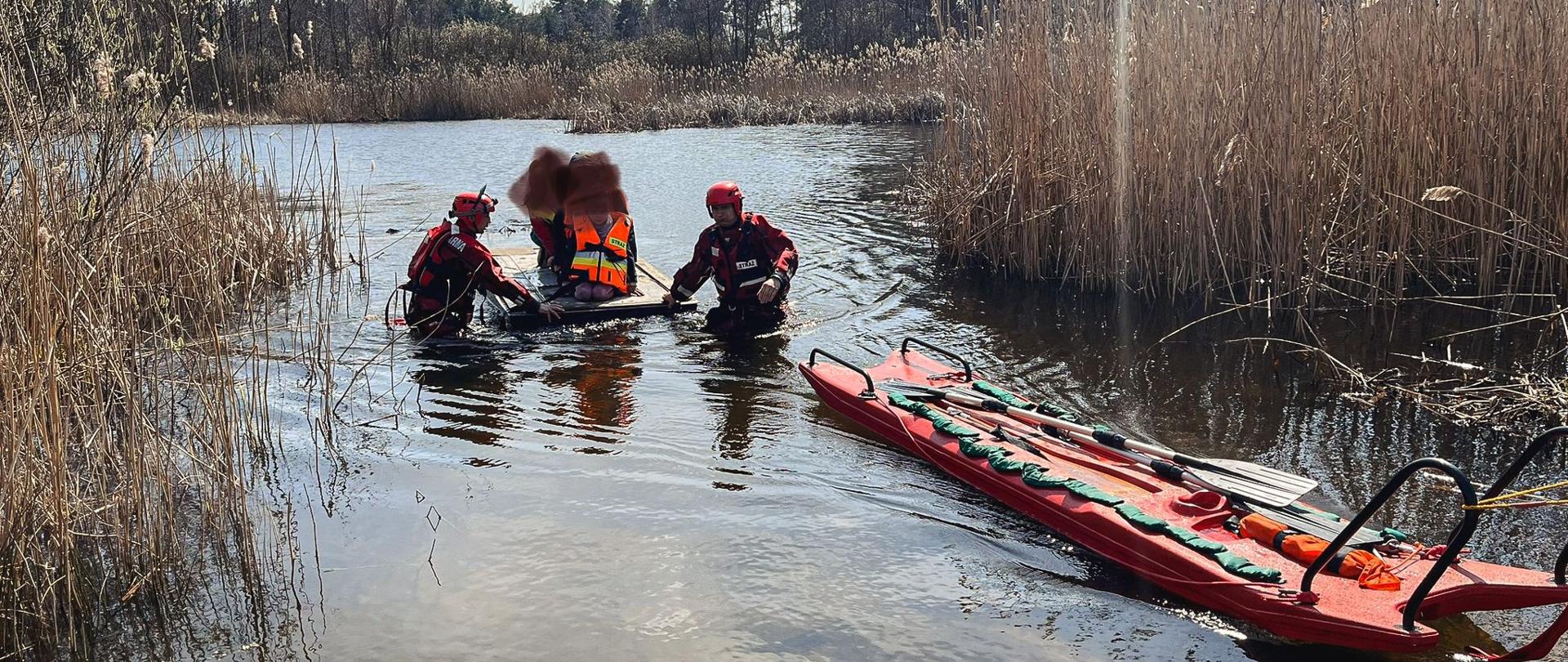 Ratownicy w ubraniach wypornościowych z wykorzystaniem sań wodno-lodowych holują tratwę z dziećmi.
