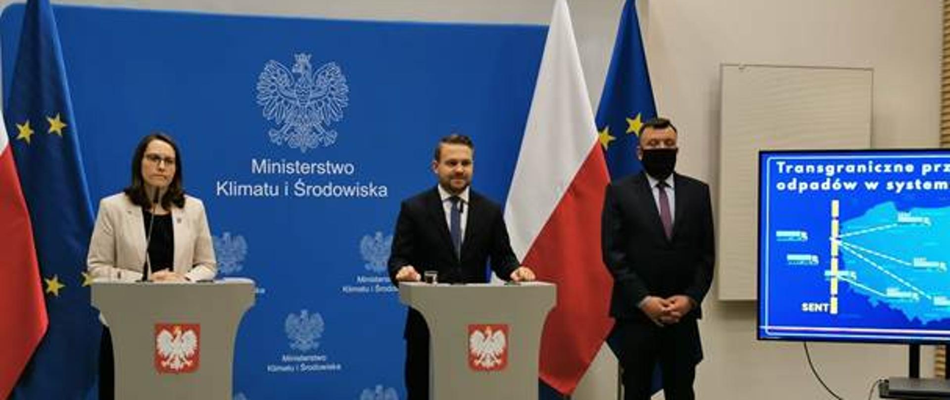 Dwie osoby stojące za pulpitami i jedna z boku