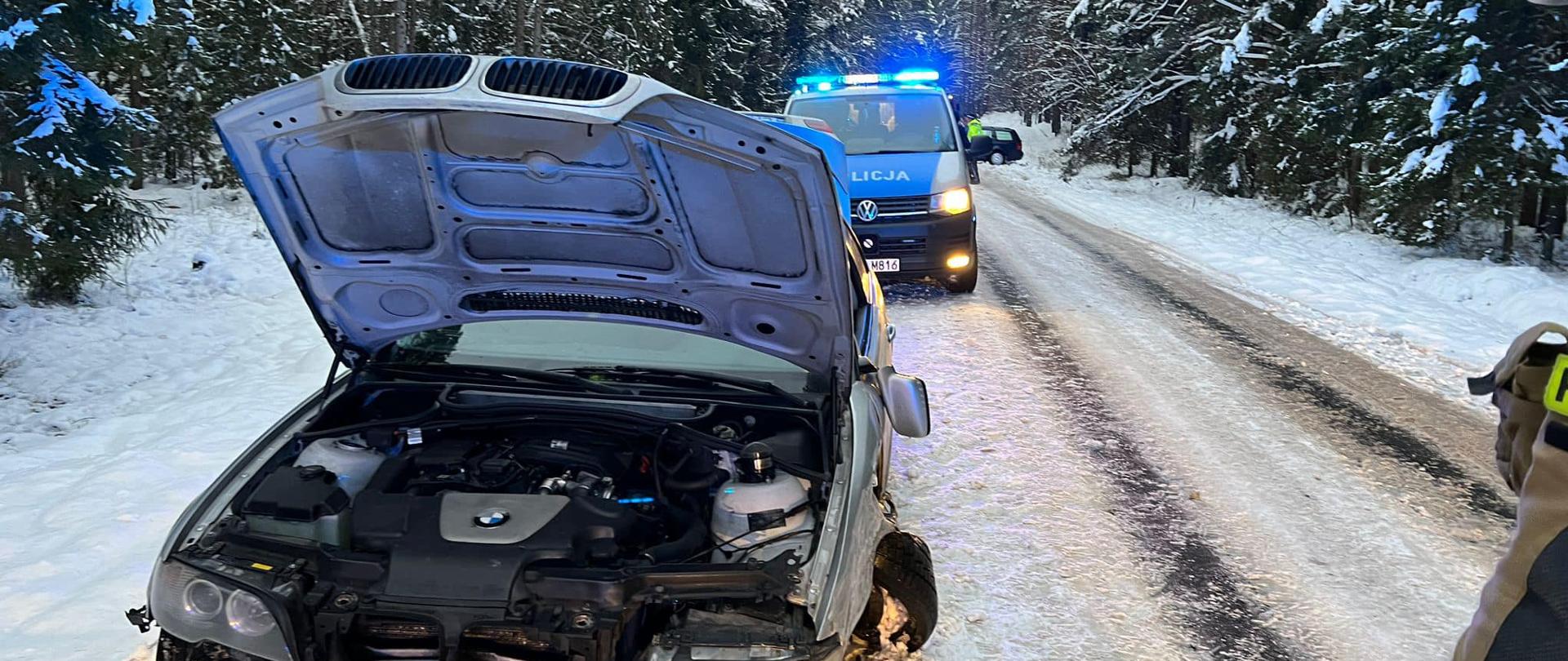 Na zdjęciu znajduje się rozbity samochód osobowy, w tle widać radiowóz oraz strażaka stojącego obok