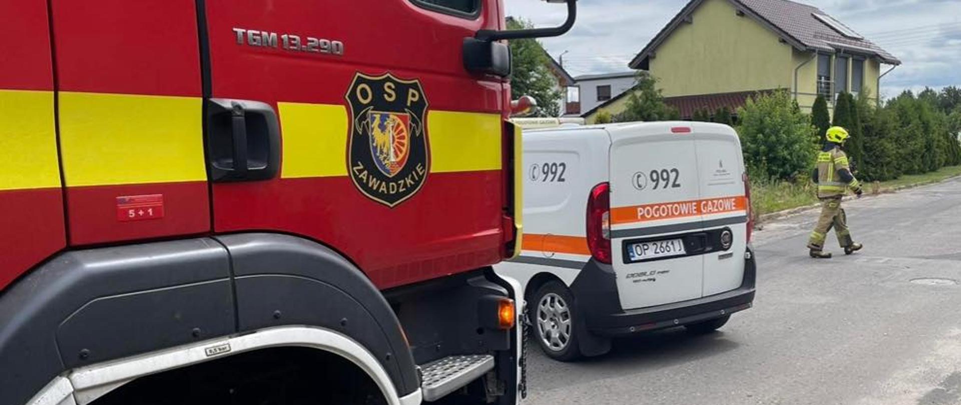 Na zdjęciu znajdują się samochód strażacki oraz pogotowia gazowego, w tle widać budynki oraz strażaka w nomexe