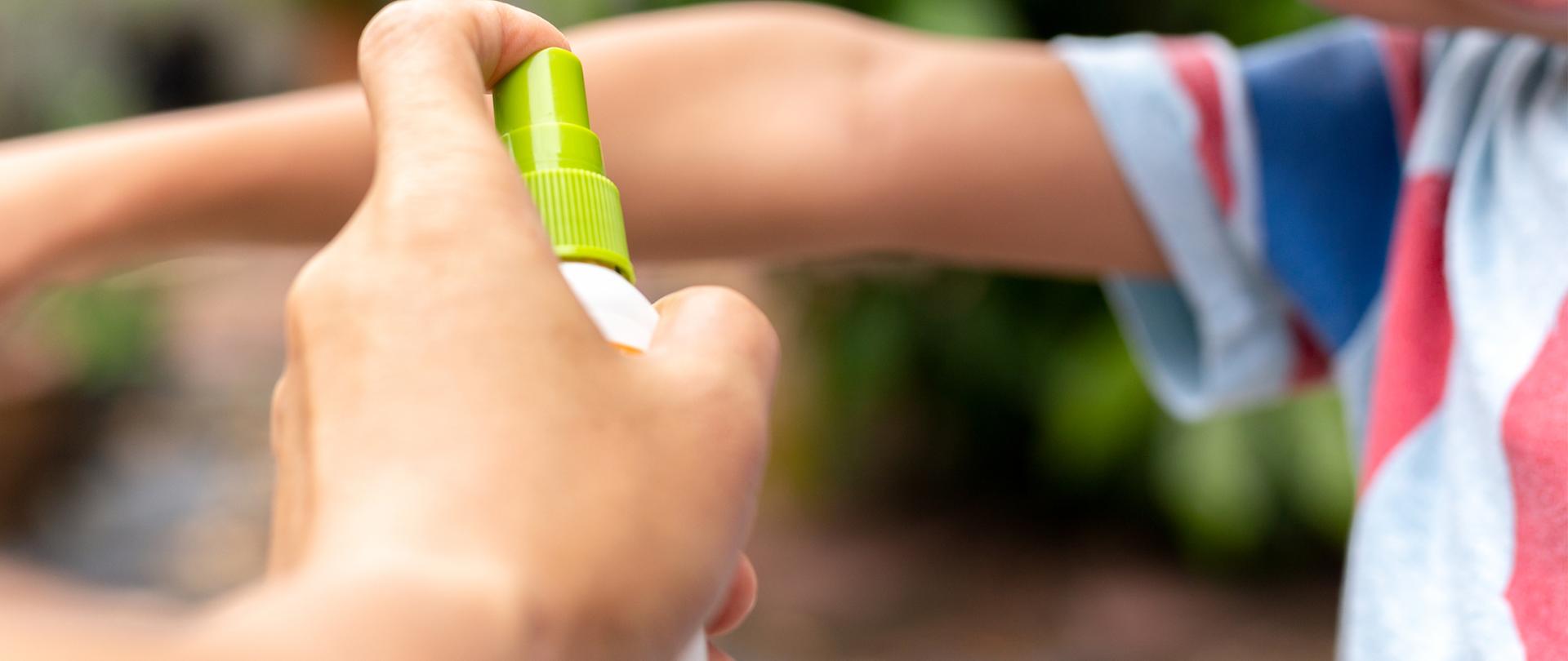 Father spraying insect repellents on his son arm in the garden
