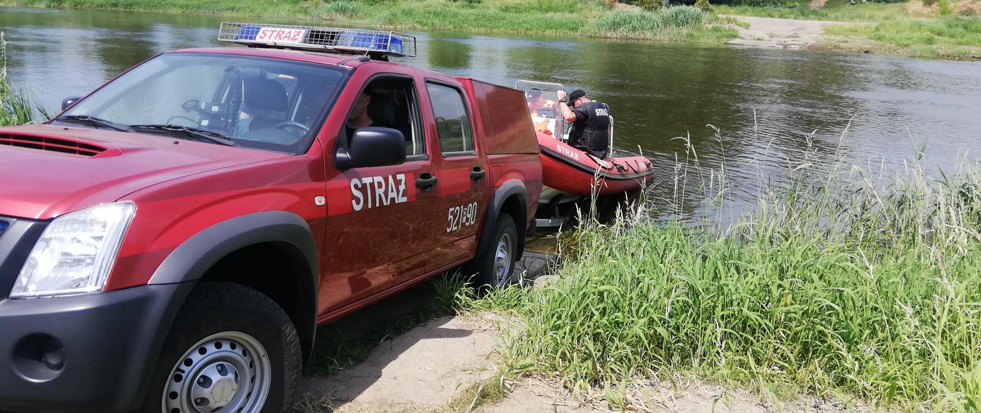 na pierwszym planie samochód strażacki cofa z łodzią do rzeki 