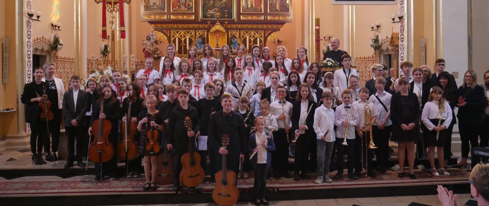Duża grupa uczniów stoi przed prezbiterium Kościoła WNMP w Wodzisławiu Śląskim, w rękach trzymają instrumenty.