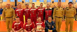 Zdjęcie przedstawia strażaków w trakcie turnieju piłkarskiego.
W tle hala sportowa.
