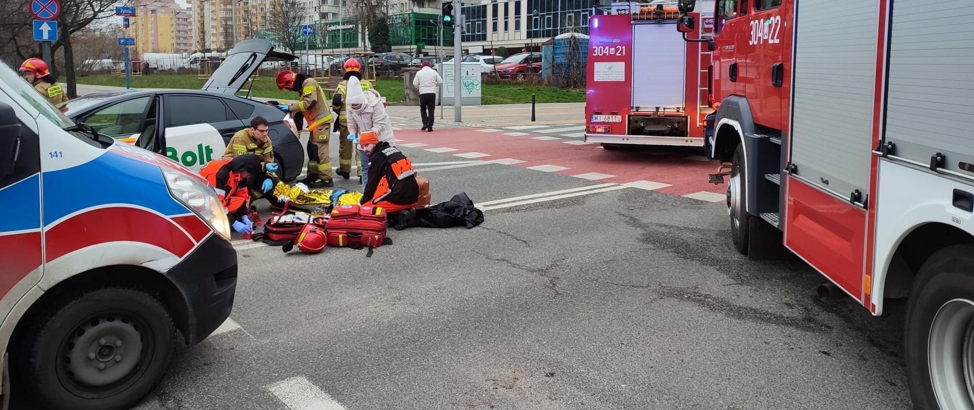 Ratownicy wykonują badanie uczestnika wypadku.