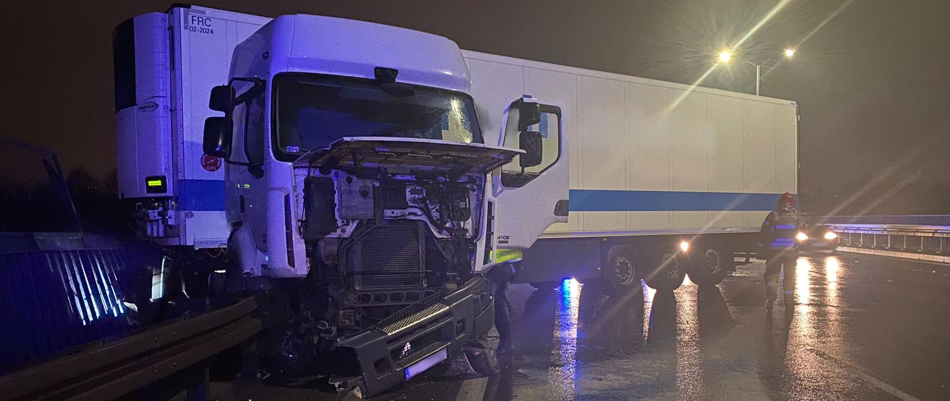 Zdjęcie przedstawia uszkodzony ciągnik siodłowy. W tle znajduje się naczepa.