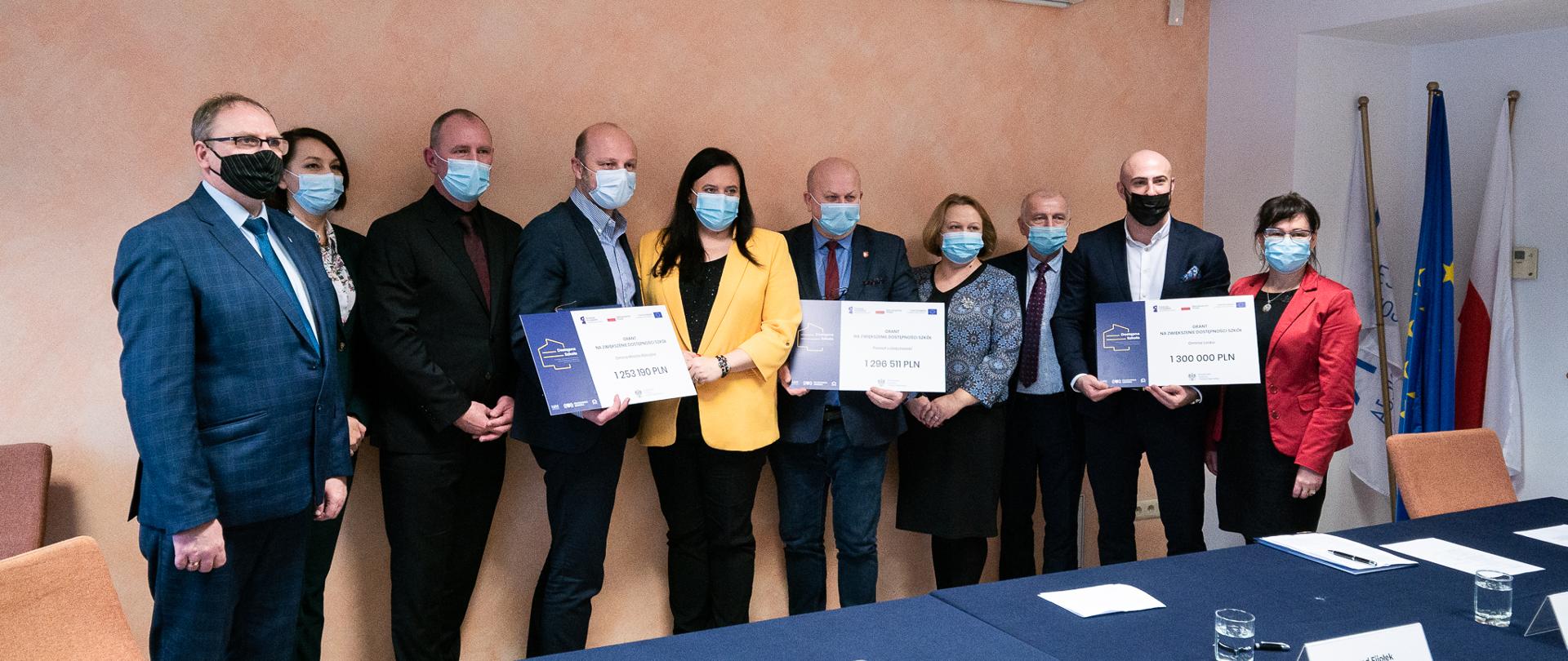 uczestnicy spotkania prezentują symboliczne czeki