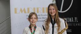 Uczennice z saksofonami na tle plakatu konkursu