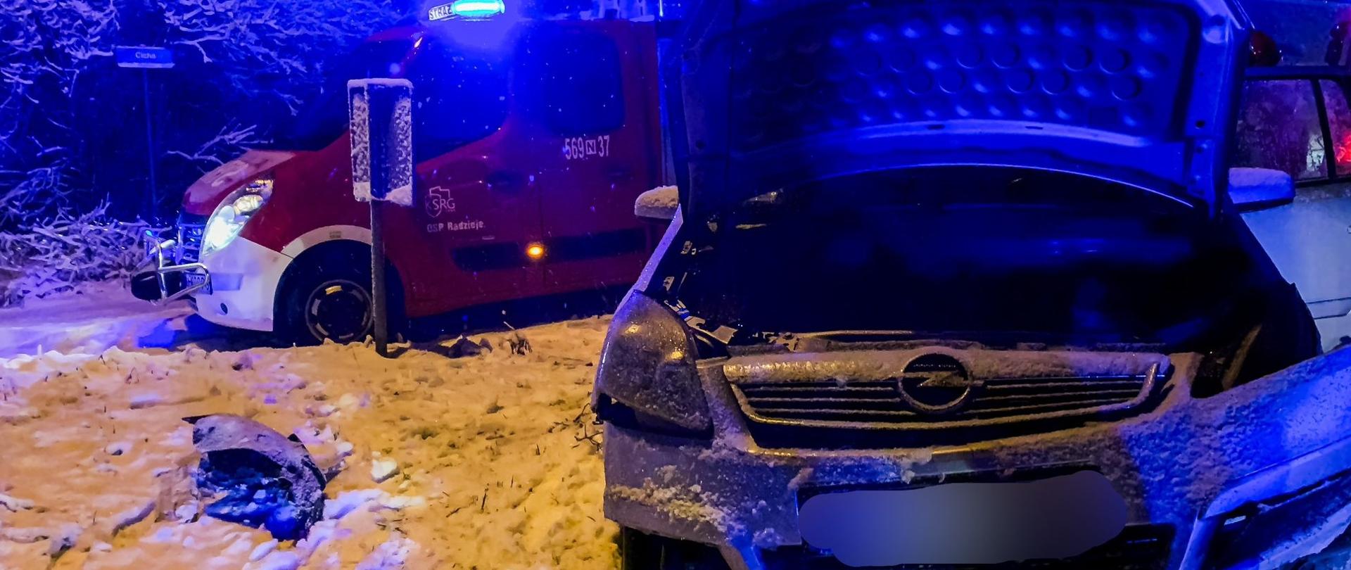 Samochód osobowy stoi na poboczu i ma rozbity przód, za nim stoi samochód ratowniczo-gaśniczy. Pora nocna. 