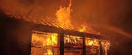 Zdjęcie przedstawia pożar słomy składowanej w stodole. Ogień strawił dach oraz bramy garażowe.