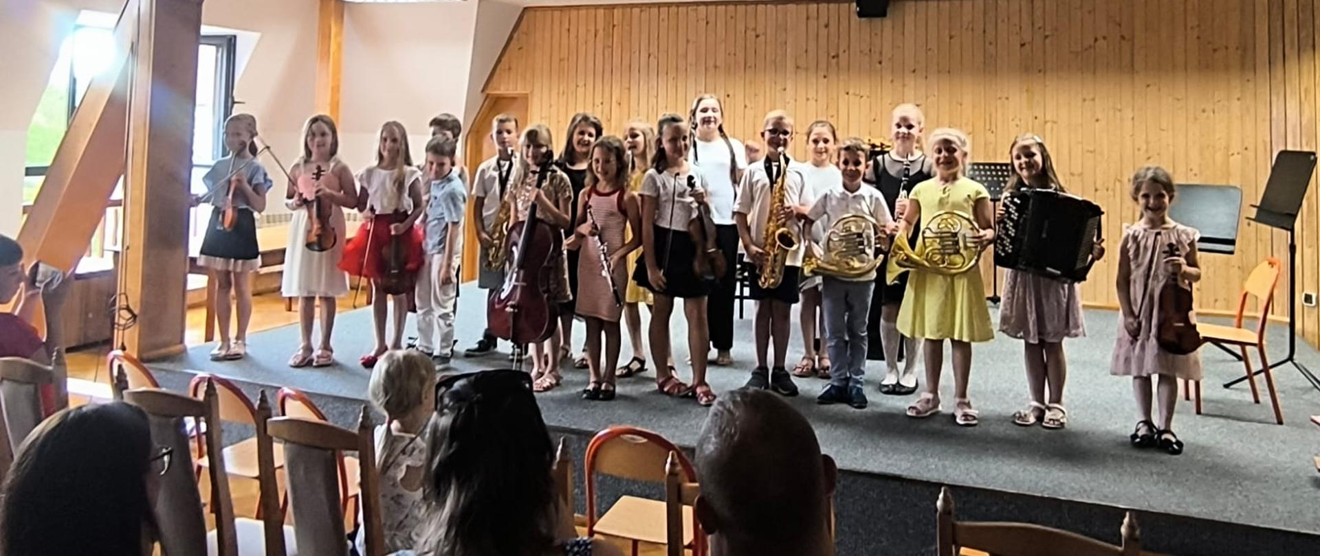 Wszyscy wykonawcy stoją ze swoimi instrumentami na scenie.