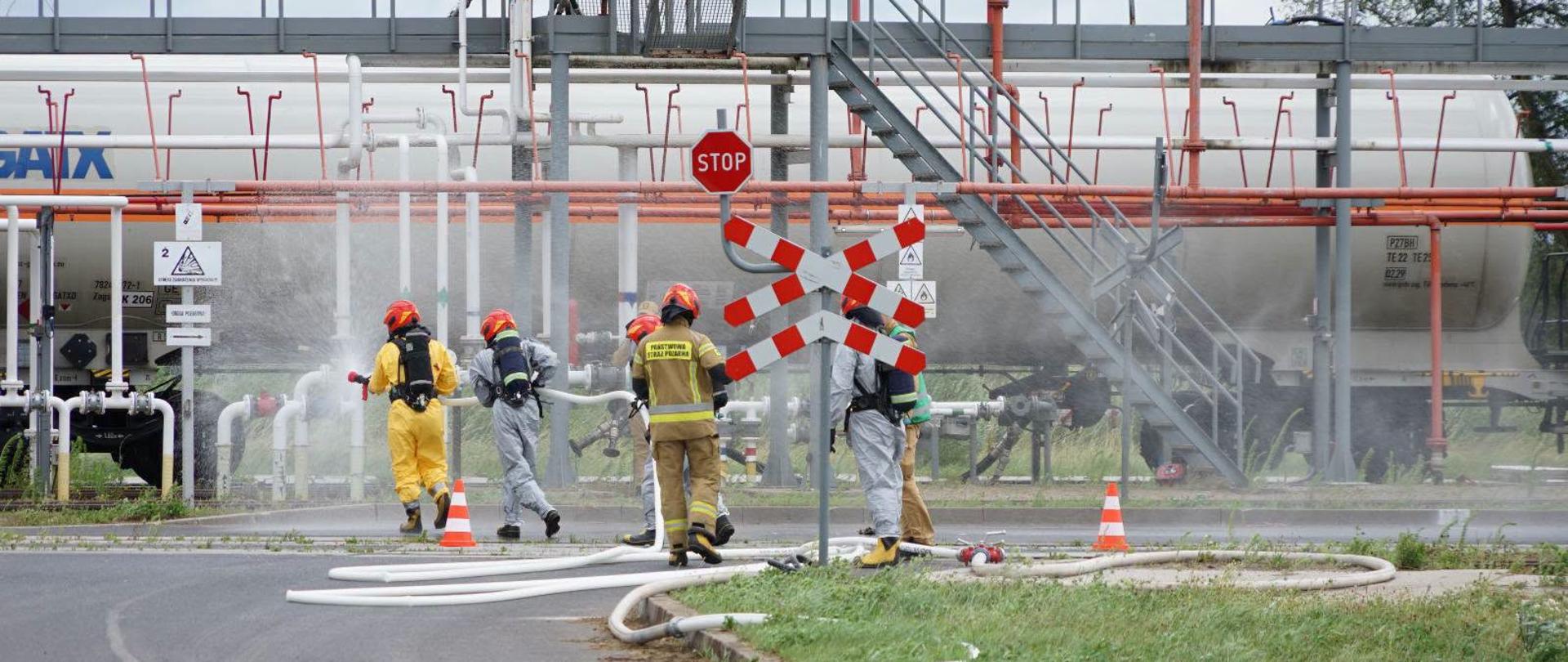 Trwają ćwiczenia na bocznicy kolejowej przeładunku gazu. Strażacy w specjalnych kombinezonach.