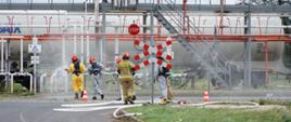 Trwają ćwiczenia na bocznicy kolejowej przeładunku gazu. Strażacy w specjalnych kombinezonach.