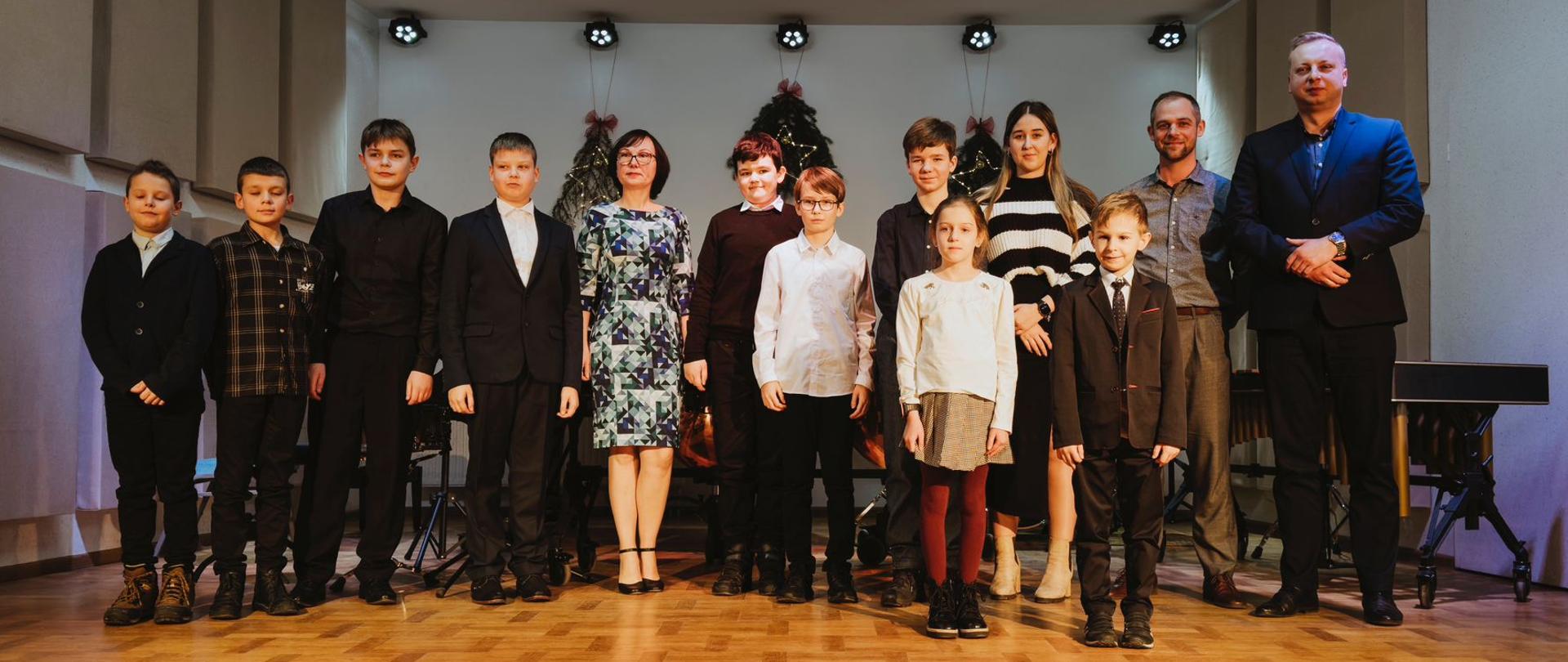 Uczniowie klasy perkusji ze swoimi nauczycielami na scenie szkoły.