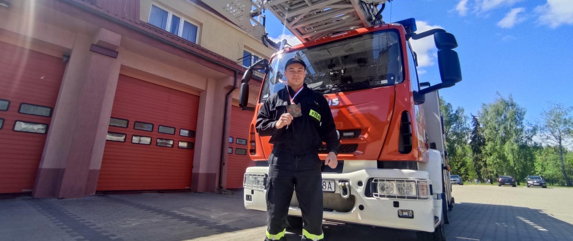 Wojciech Barszczewski stojący z medalem przy drabinie mechanicznej na JRG 1 w Suwałkach