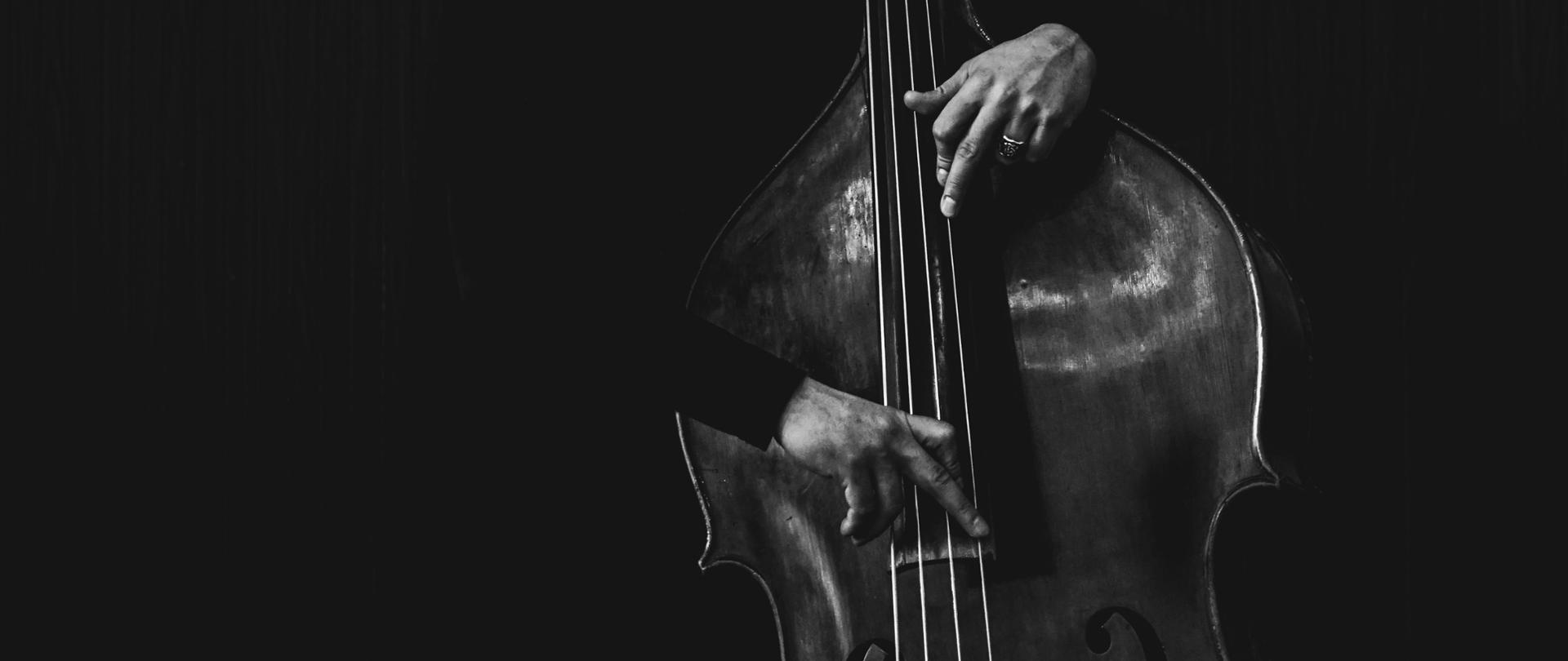 fotografia czarno-biała przedstawiająca kontrabas oraz dłonie mężczyzny ułożone na strunach