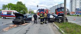 Na zdjęciu widzimy kolizję drogową dwóch samochodów osobowych: Audi A4 oraz Volkswagen Passat CC. Z lewej strony zdjęcia samochód Audi A4 ma uszkodzony prawy bok pojazdu. Po prawej stronie zdjęcia widzimy samochód Passat, który uderzył w przydrożny słup oświetleniowy. Pojazd ma uszkodzony przód. W dalszym tle zdjęcia widzimy Zespół Pogotowia Ratunkowego oraz strażackie pojazdy. Siła zderzenia dwóch pojazdów osobowych była tak duża, że na ulicy widać porozrzucane elementy karoserii obu pojazdów. Z samochodu Audi na pas drogowy wyciekły płyny eksploatacyjne, które zostały zneutralizowane przez strażaków sorbentem Compact.