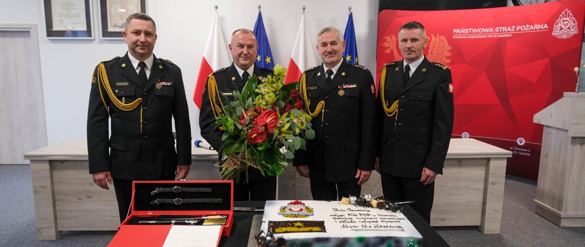 Kierownictwo KP PSP w Gdańsku. Po środku stoi nadbryg. Jacek Niewęgłowski z kwiatami. Przed komendantami atrybuty generalski oraz tort.