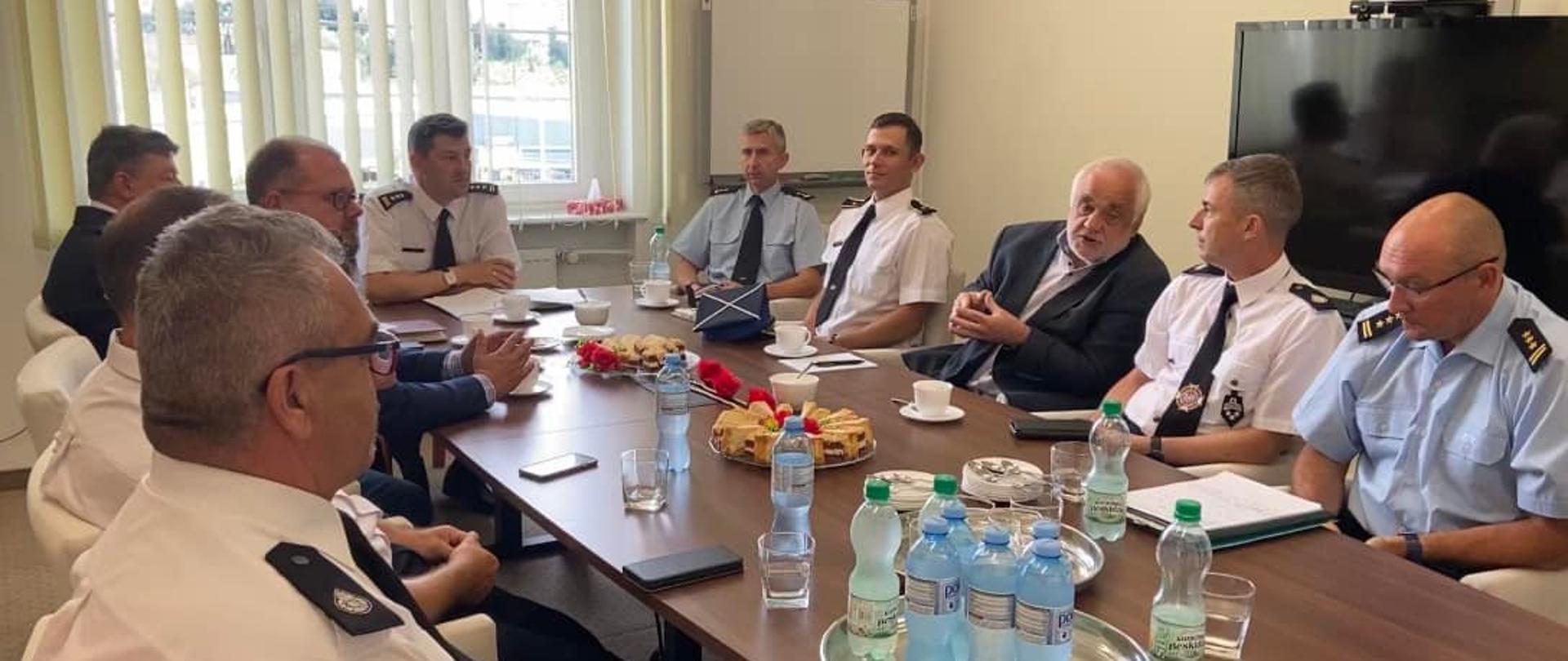 Zdjęcie przedstawia Spotkanie w KW PSP Szczecin. Strażacy OSP i PSP siedzą przy stole oraz rozmawiają.