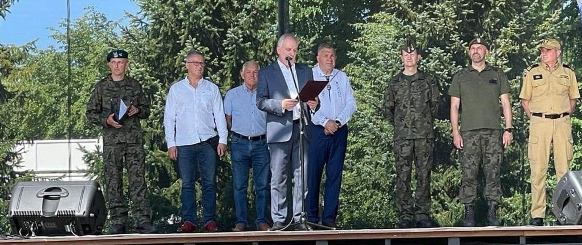 Wojewoda pomorski czyta list za nim stoją przedstawiciele wojska Państwowej Straży Pożarnej oraz władz samorządowych. 
