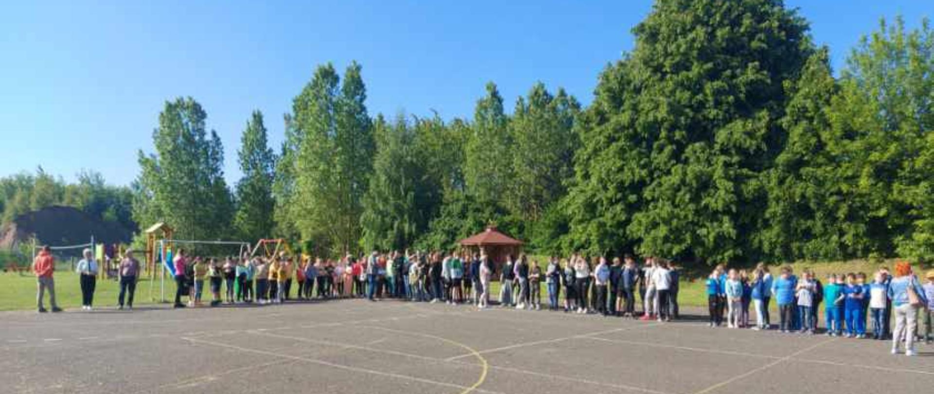 Dzieci oraz pracownicy placówki oświatowej stoją na boisku w trakcie ewakuacji.